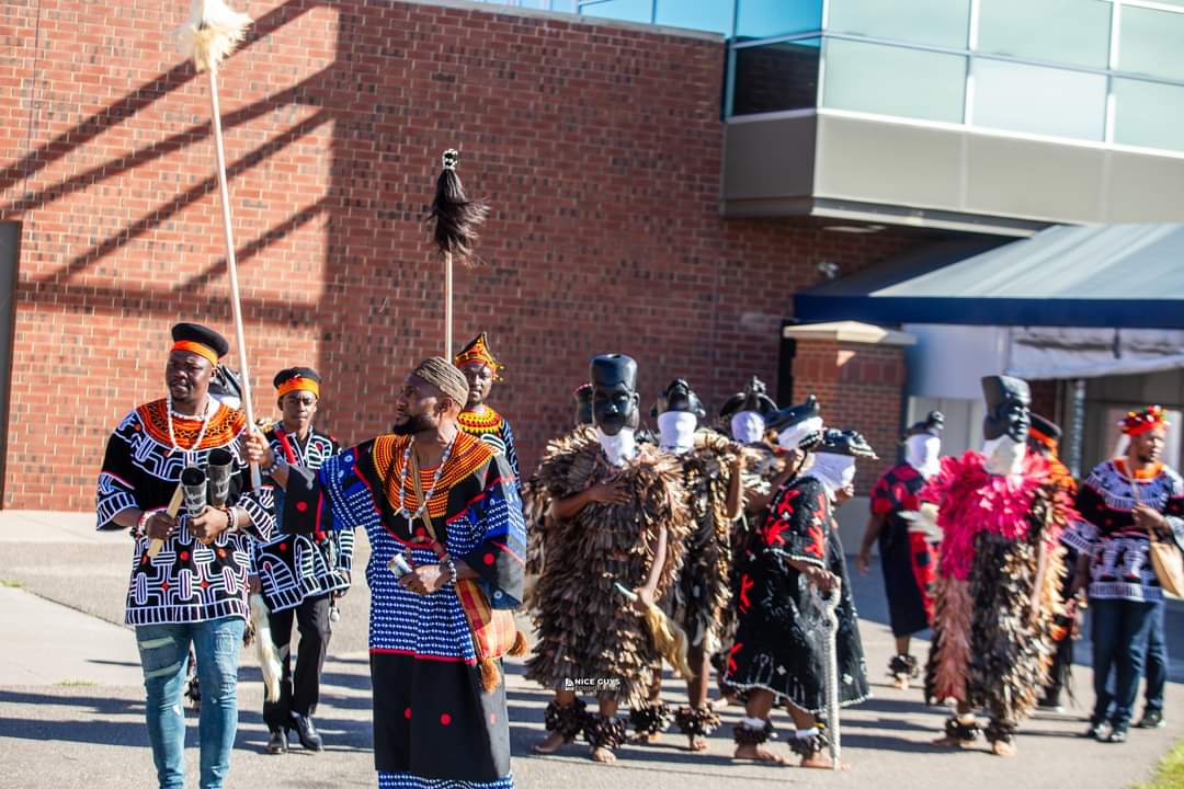 A full masked juju group in traditional regalia processes outdoors alongside drummers and elders at a BotangRecords cultural event.