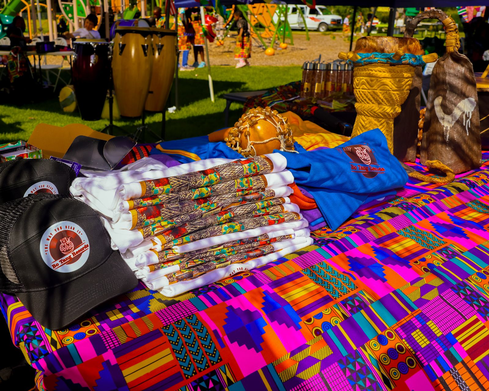 BotangRecords caps and printed shirts on a kente-covered table beside traditional instruments