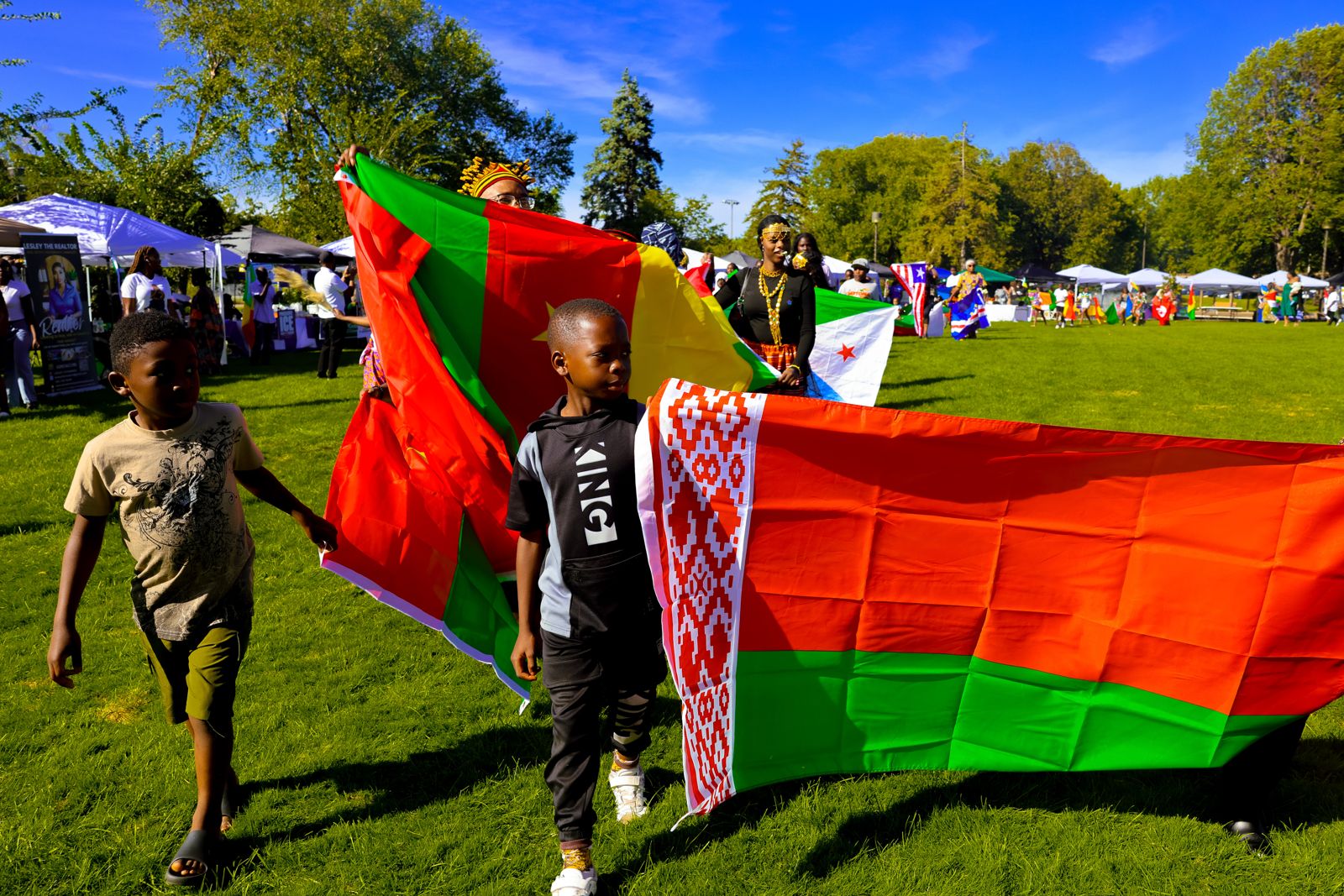 Children and adults carrying the Cameroon flag and other national flags across the park